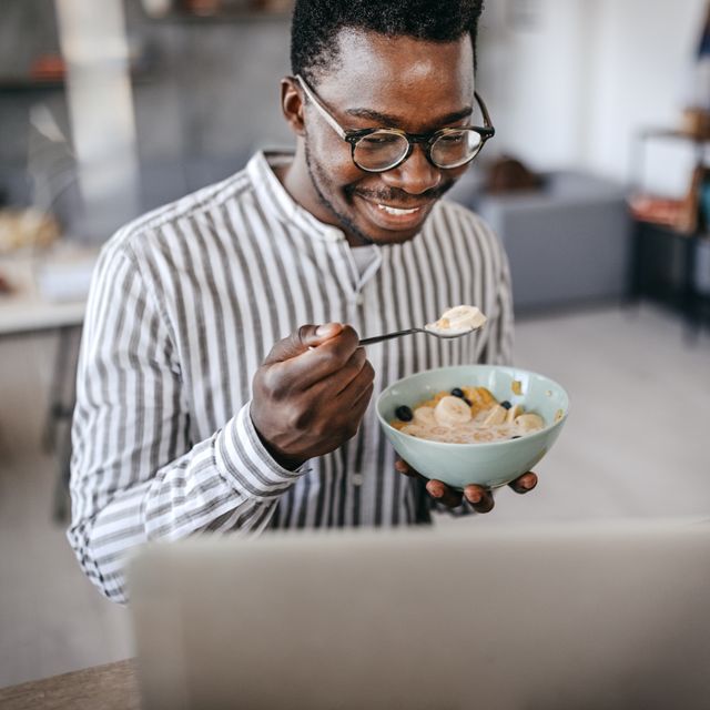 man eating breakfast and using laptop