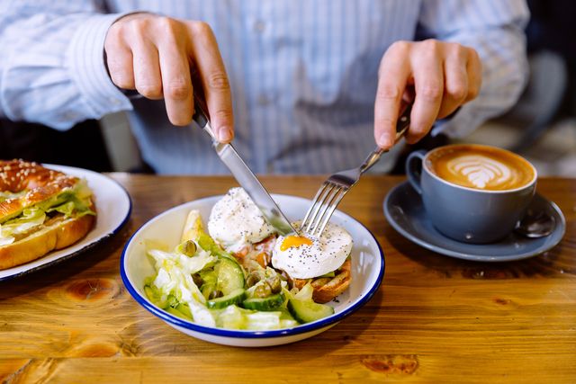 man eating breakfast with poached eggs, fresh salad and coffee