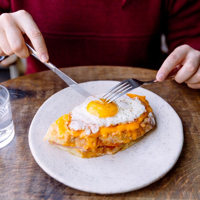 man eating croque madame sandwich with cheese and fried egg