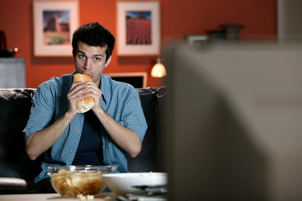 man eating sandwich and watching television