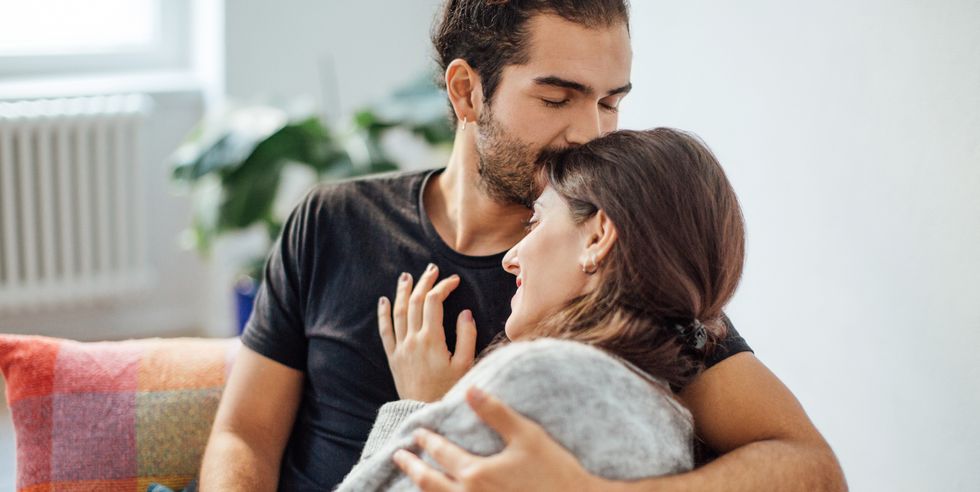 man embracing girlfriend while kissing on her forehead at home