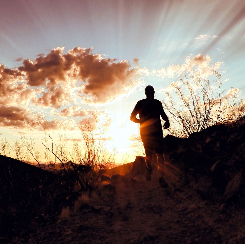 sunrise with rays of light spreading through the clouds while a man runs towards the edge of the hill