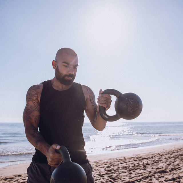 Man Exercising With Kettlebells At Beach Against Sky