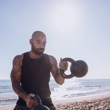 man exercising with kettlebells at beach against sky