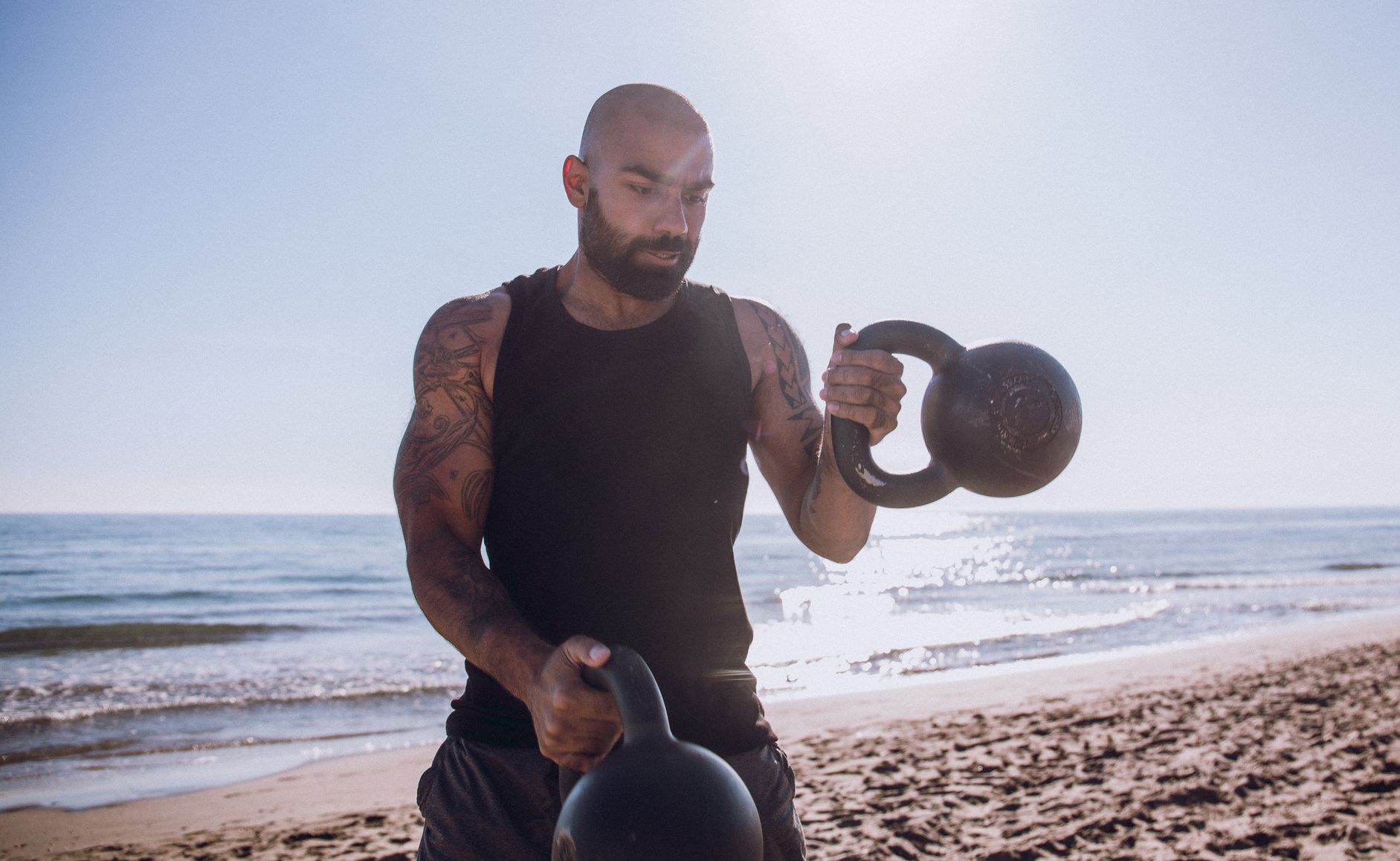 man exercising with kettlebells at beach against sky