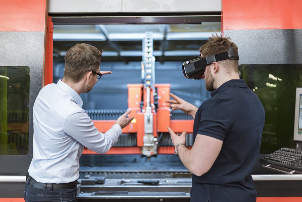 Man explaining machine to colleague wearing VR glasses in factory