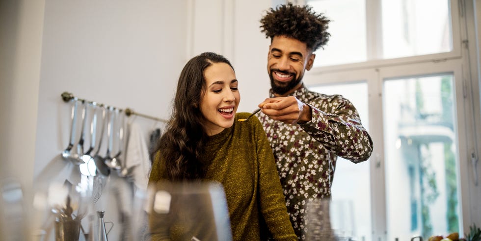 young man feeding pumpkin soup to girlfriend in kitchen at home