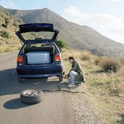 Man fixing flat tire, car packed for road trip