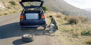 Man fixing flat tire, car packed for road trip