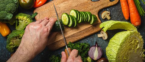 man hands chopping cucumber on wooden cutting board with knife and
