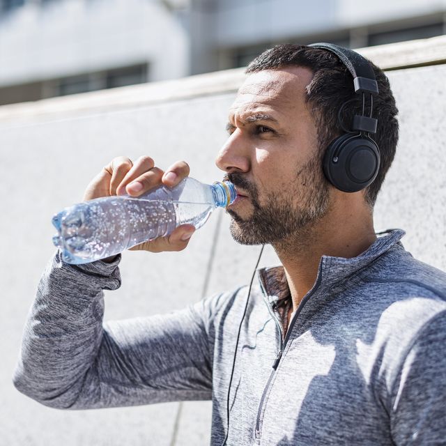 Man having a break from exercising wearing headphones and drinking from bottle