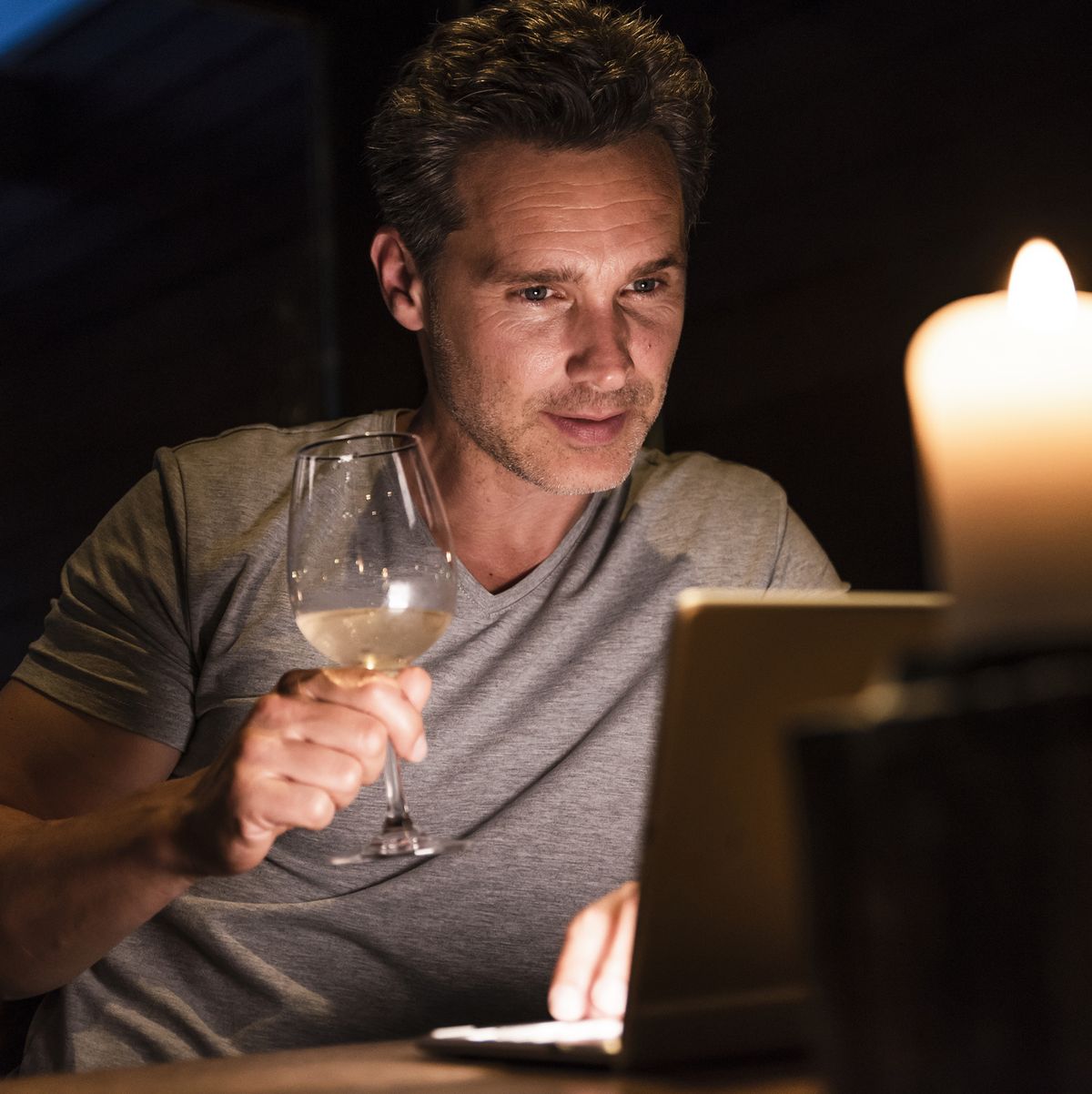 Man having glass of white wine looking at laptop