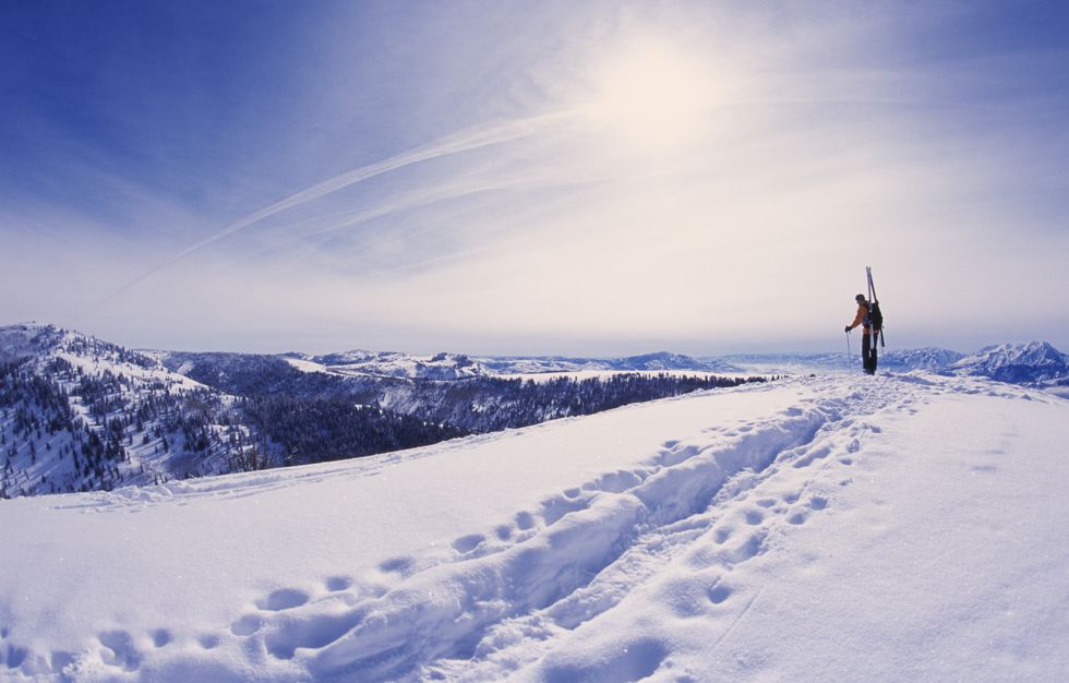 man hiking with skis through snow in mountains