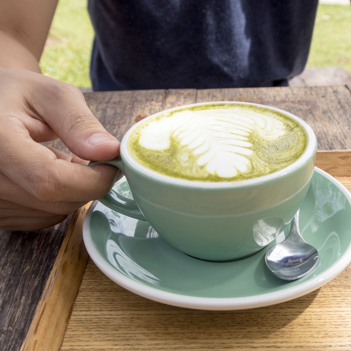 man holding a cup of hot green tea latte on wooden table.