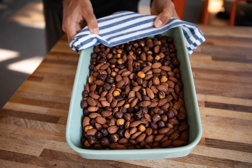 a man holding an ovenware full of roasted hazelnuts and almonds
