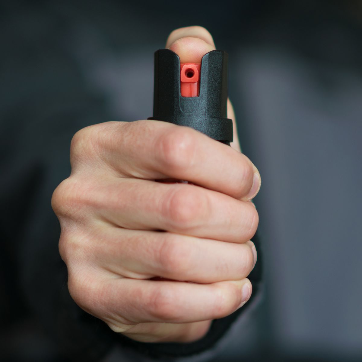 man holding pepper spray tear gas in his hand self defense blur background, close up