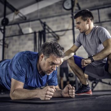 Man holding plank in a gym with trainer watching