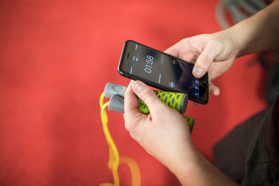 man holding skipping rope and phone to time intervals during a workout