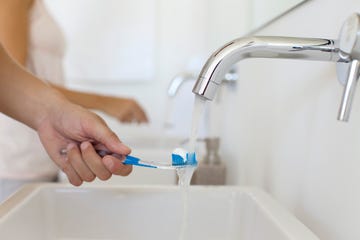 man holding toothbrush under faucet, cropped