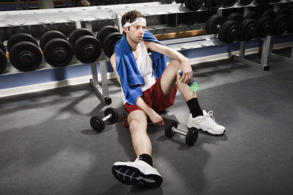 man holding water bottle sitting on gym floor by weights