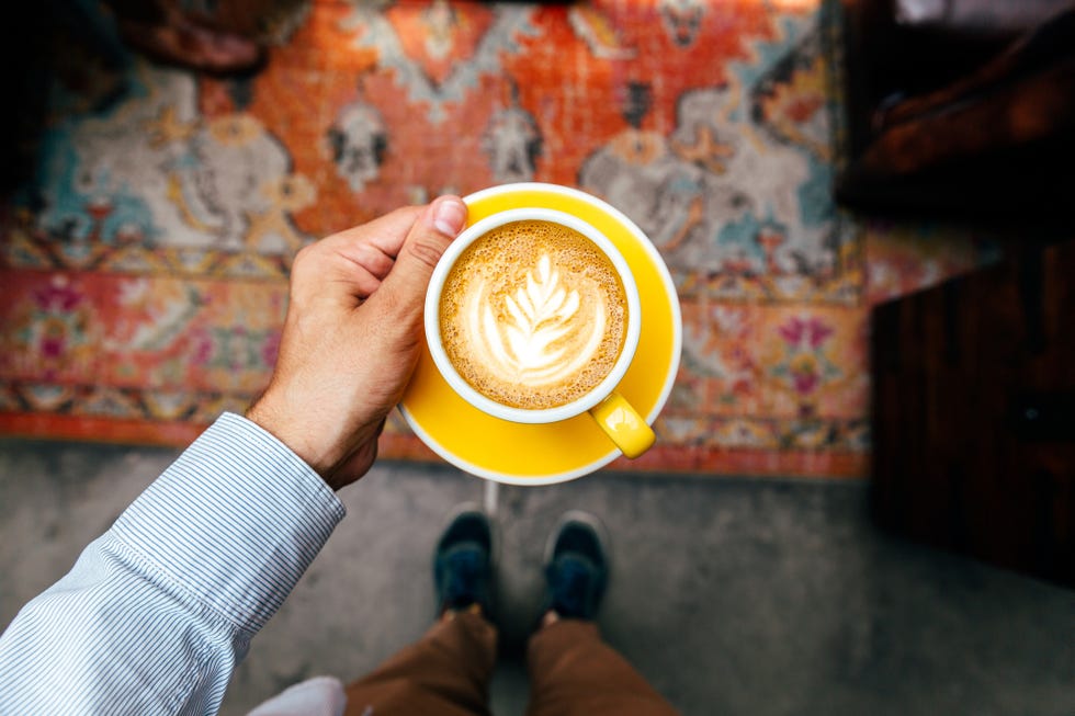 man holding yellow cup with cappuccino, personal perspective view