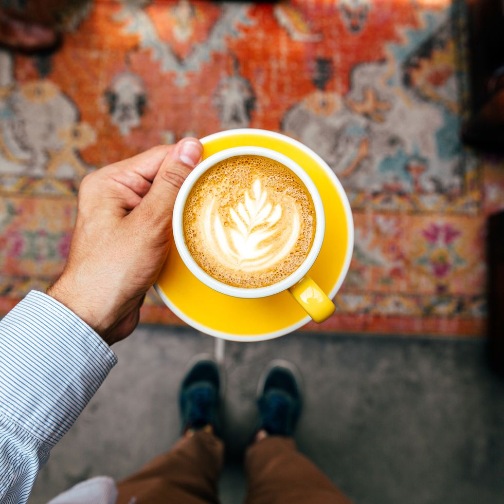 man holding yellow cup with cappuccino, personal perspective view