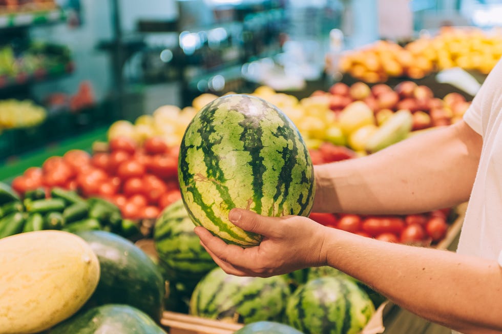 a man holds a watermelon in his hands in a supermarket