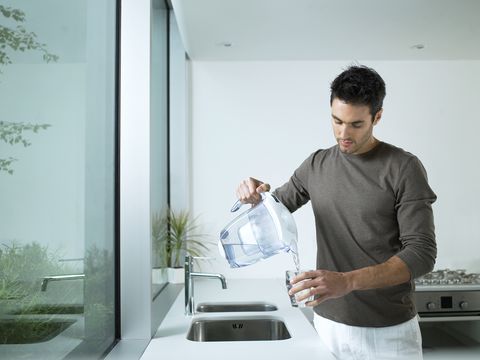 man in kitchen pouring glass of filtered water