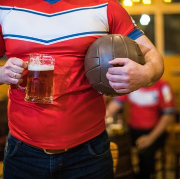 Man in sports uniform holding a beer glass and a ball in a bar