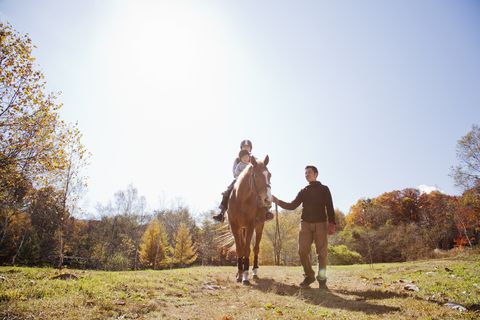man leading mother and son who are riding on horse in pasture