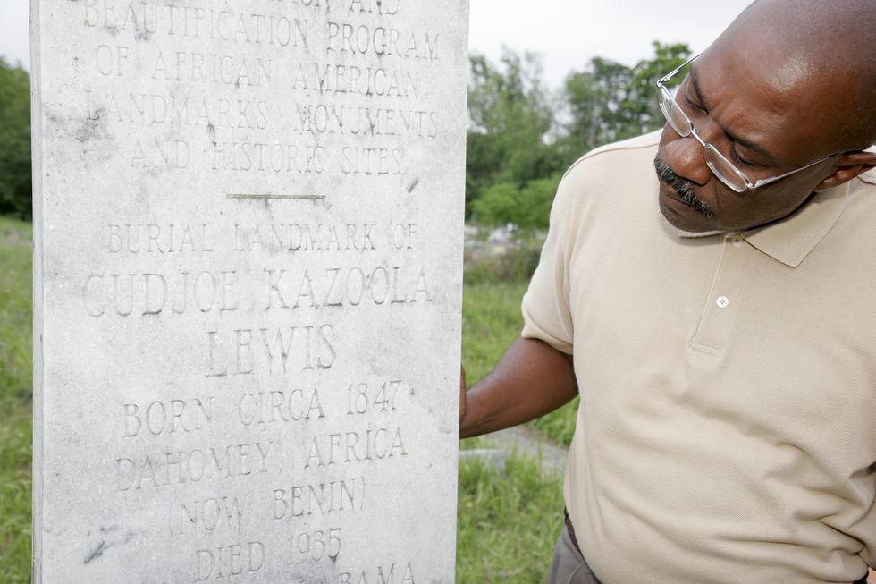 a man looking at cudjoe kazoola lewis gravestone in the cemetery at the africa town, welcome center