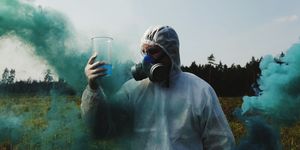 Man Looking At Liquid In Container While Wearing Gas Mask On Field Against Sky
