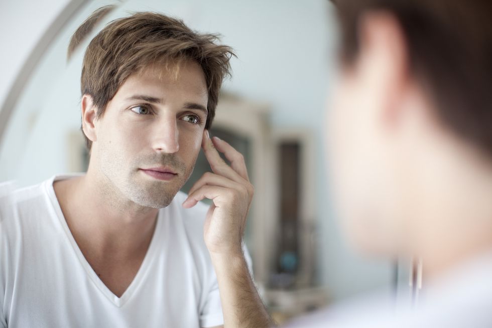 man looking at self in mirror with concern about his complexion