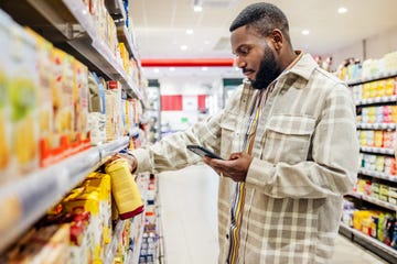 man looking at smartphone while choosing items in supermarket