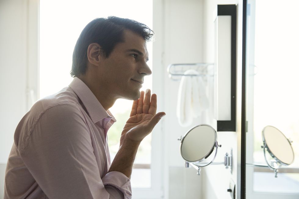 man looking in mirror, applying moisurizer to face