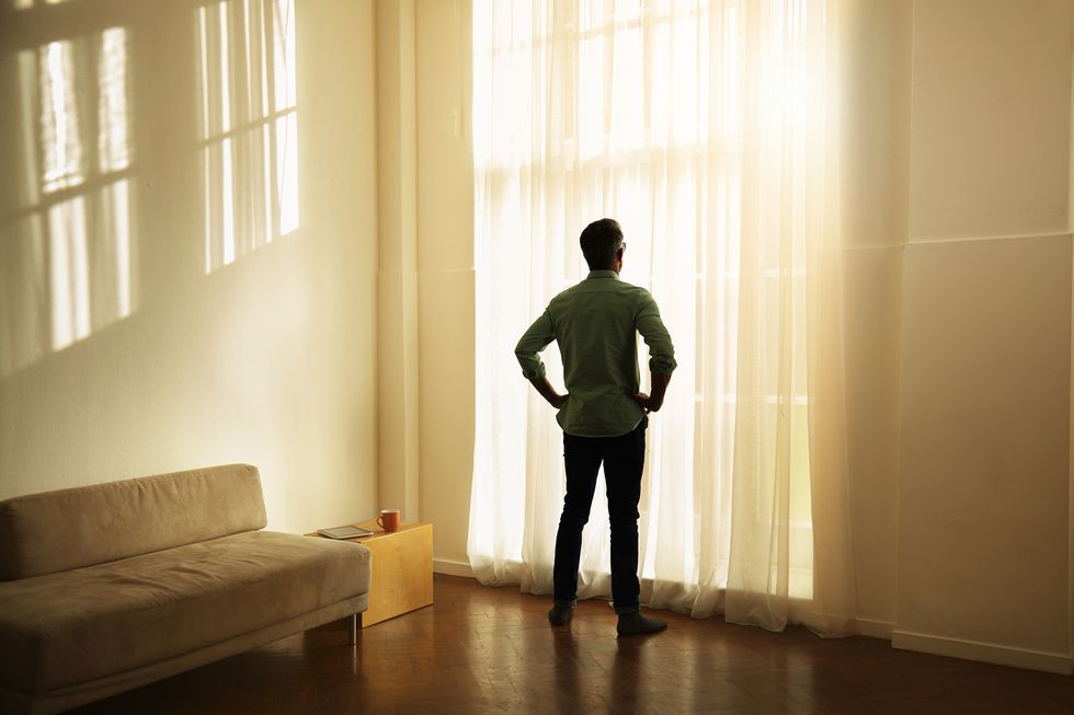 man looking out of apartment at sunrise