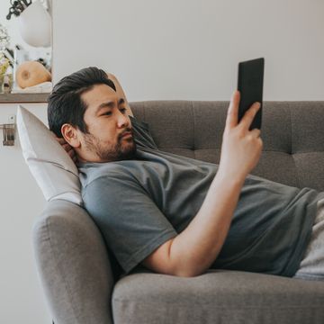 a man reads an ebook while lying on a sofa with one arm behind his head for support