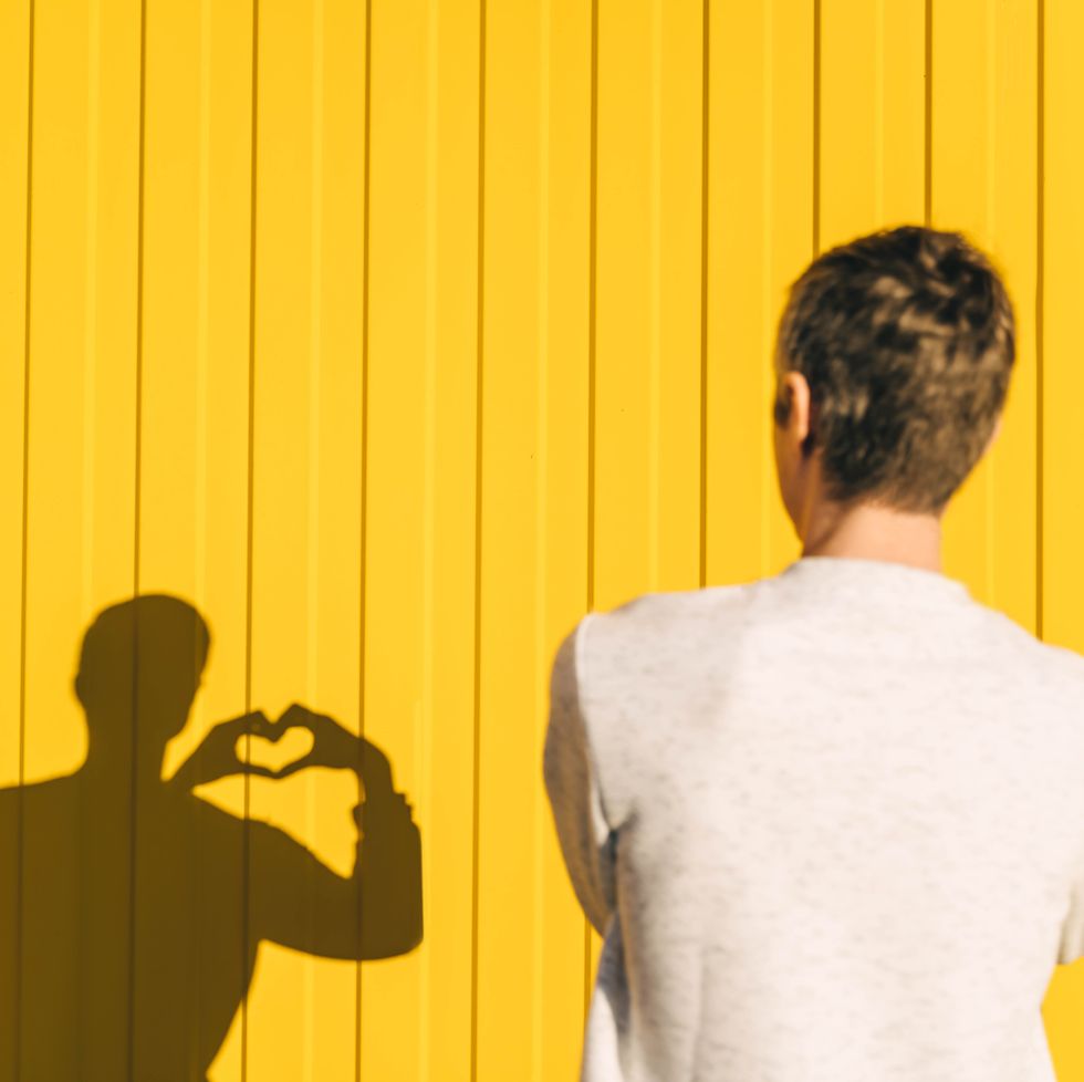 man makes heart shape with hand on yellow background, rear view