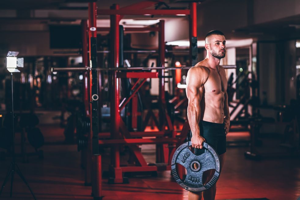 young caucasian handsome muscular man holding weight disk in gym