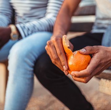 man pealing orange while sitting with a friend on the bench