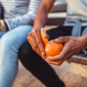 man pealing orange while sitting with a friend on the bench