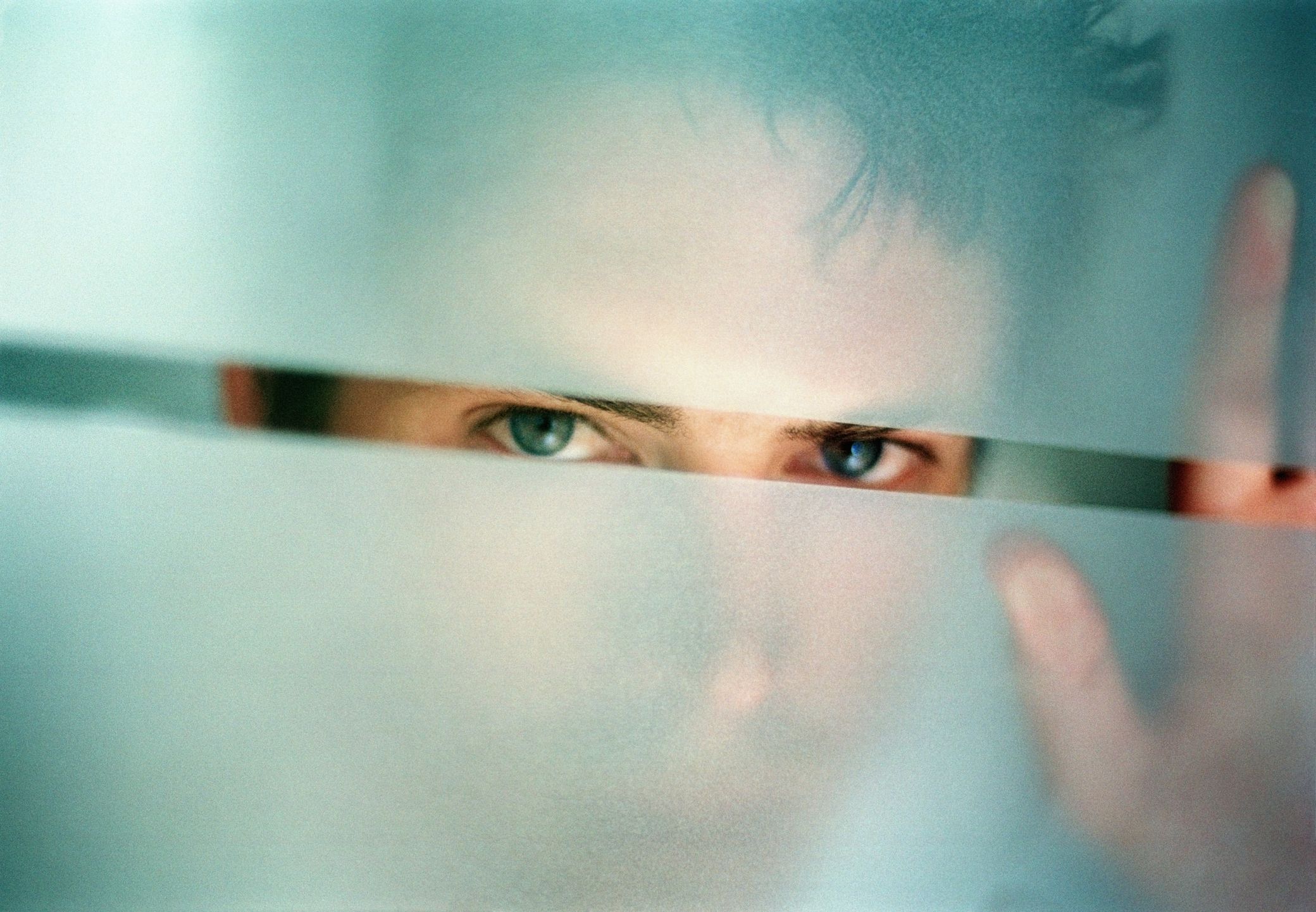man peering through gap in frosted glass, portrait, close up