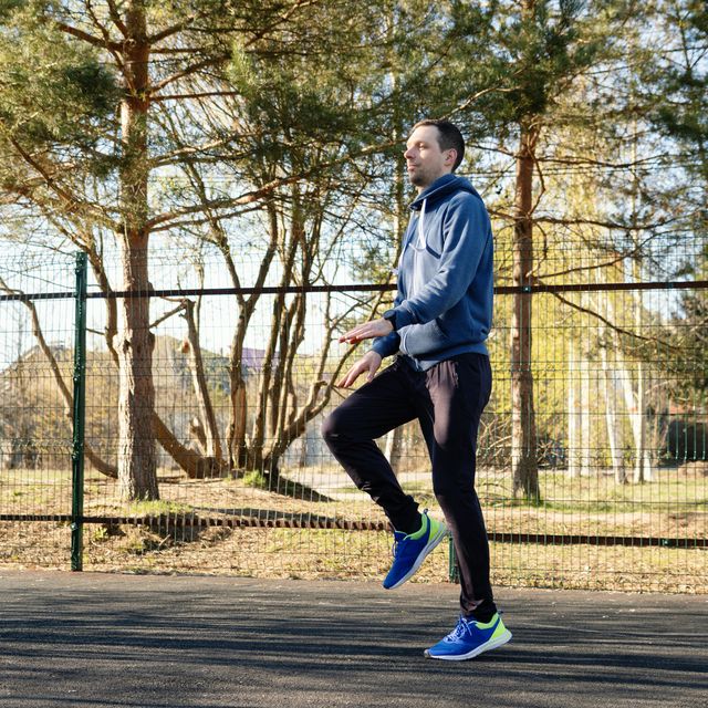 man performing high knee warm up exercises in sunny outdoor park