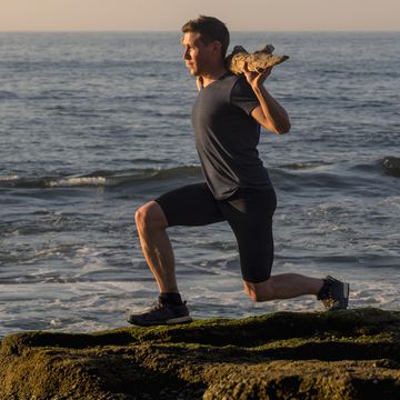 man performing squat exercise using wooden log at azkorri beach