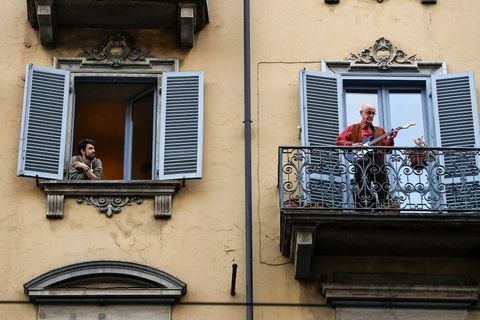 A man plays guitar from the balcony of his home as a man...