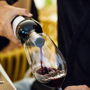 man pouring red wine in glass during dinner party