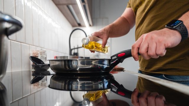 a man pours cooking oil into a frying pan while cooking a meal