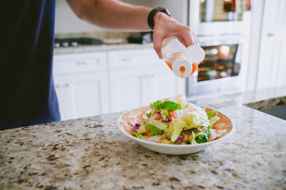 man pours salad dressing onto salad