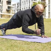 man practicing plank position on exercise mat in public park