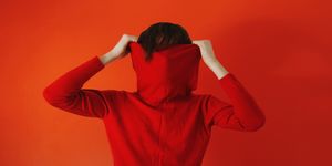 Man pulling red sweater over face against red background